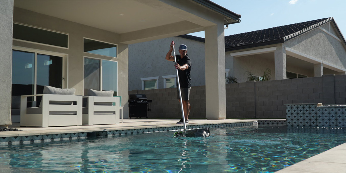 Pool maintenance employee skimming a Scottsdale swimming pool